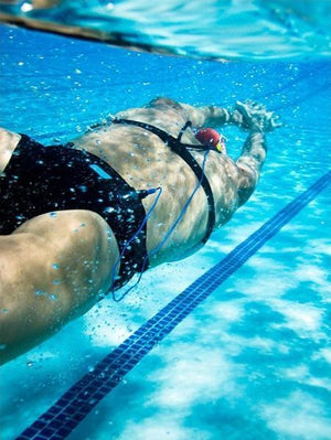 A female swimmer is streamlined underwater while listening to music from a waterproof phone case and headphones made by H2O Audio. 